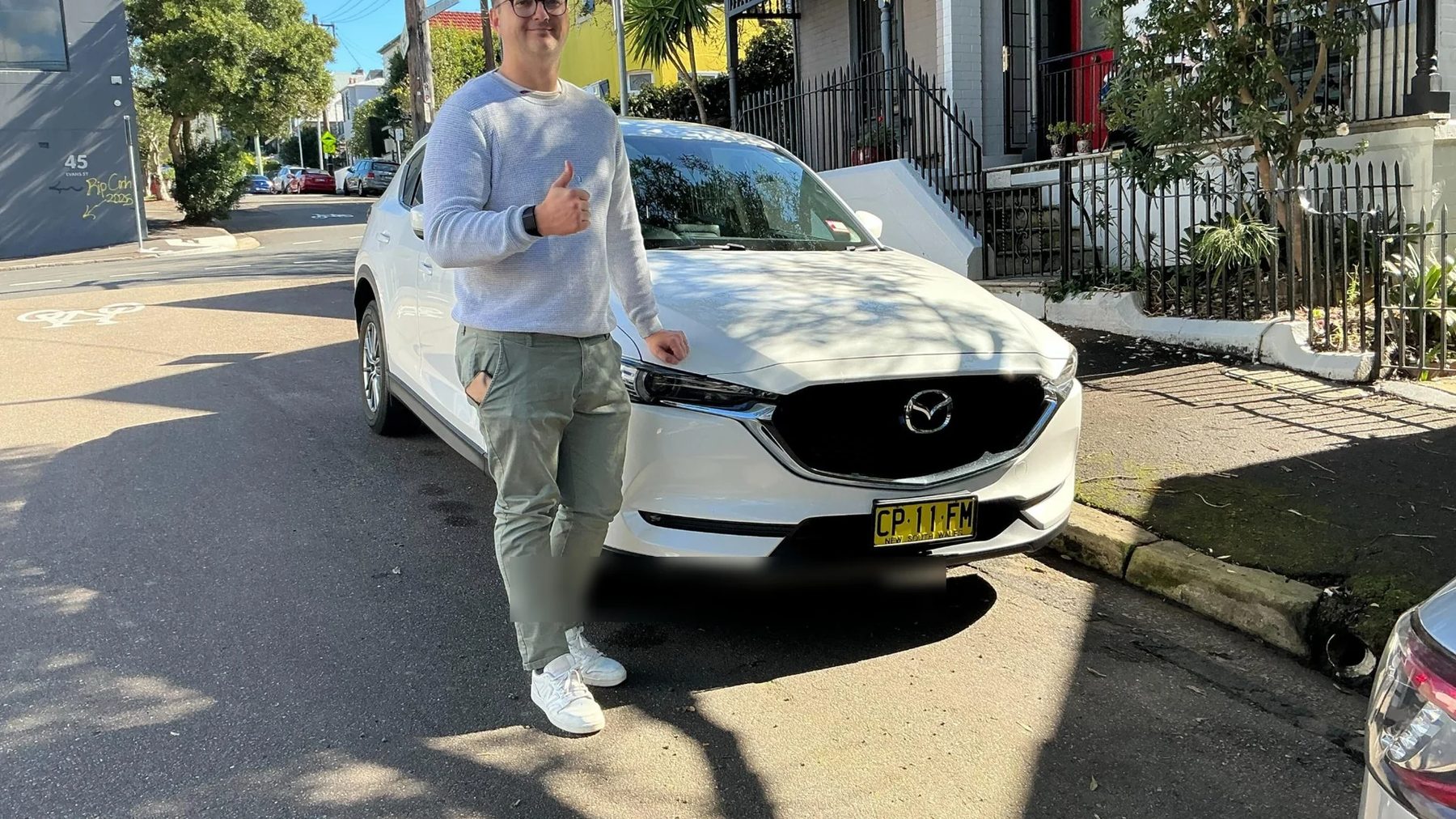 A CarBuyers customer giving a thumbs up next to the white Mazda CX-5 they just sold